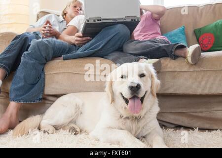 Family using laptop on couch, pet dog in foreground Stock Photo