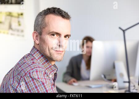 Side view of mature man in office looking at camera smiling Stock Photo