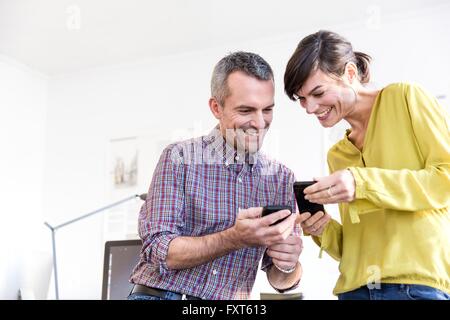 Low angle view of colleagues in office looking at smartphones smiling Stock Photo