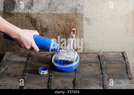 Hand pouring paint into plastic container with paint brush Stock Photo