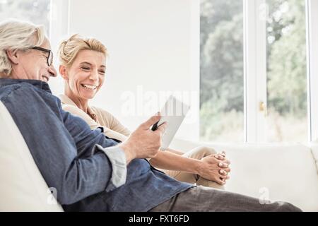 Couple relaxing on sofa, looking at digital tablet