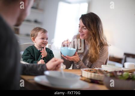 Parents at dining table feeding smiling baby boy Stock Photo