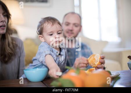Parents having lunch with baby boy, peeling orange Stock Photo