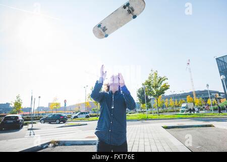 Young male urban skateboarder throwing skateboard mid air Stock Photo