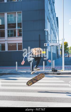 Young male urban skateboarder doing skateboard jump  on pedestrian crossing Stock Photo