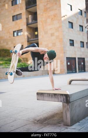 Young male skateboarder doing balance skateboard trick on urban concourse seat Stock Photo
