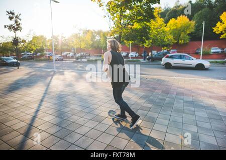 Young male urban skateboarder skateboarding along sidewalk Stock Photo