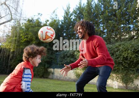 Father and son playing with football in garden smiling Stock Photo