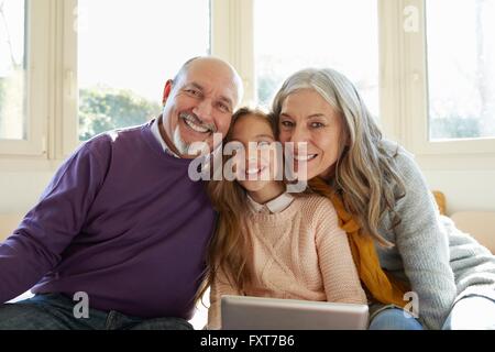Grandparents on window with granddaughter holding digital tablet looking at camera smiling Stock Photo