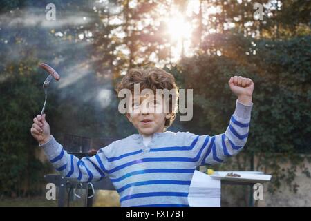 Boy arms raised holding sausage on fork smiling Stock Photo