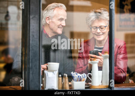 Senior couple in cafe window seat drinking coffee and texting on smartphone Stock Photo