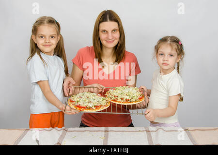 Mom and two small daughters show the two had not yet made baked pizza on a baking sheet Stock Photo