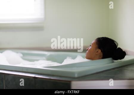 Young woman relaxing in bubble bath gazing through window Stock Photo