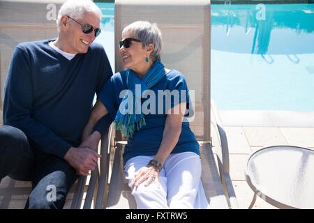 Senior couple relaxing on sun loungers beside pool Stock Photo