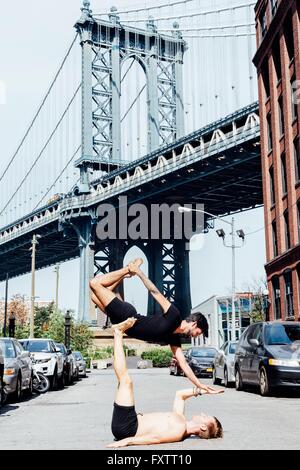 Man balancing on top of another in yoga position by Manhattan Bridge, New York, USA Stock Photo