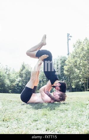 Two men poised in face to face yoga position in park Stock Photo