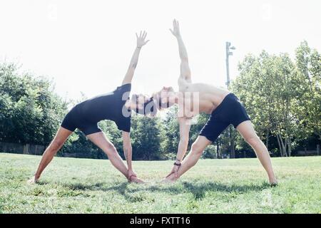 Two men poised in leaning sideways yoga position in park Stock Photo