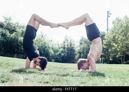 Two men poised upside down in yoga position in park Stock Photo