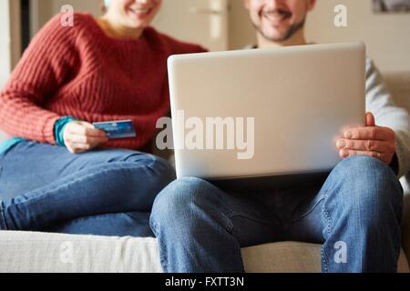 Cropped view of couple sitting on sofa using laptop and credit card Stock Photo