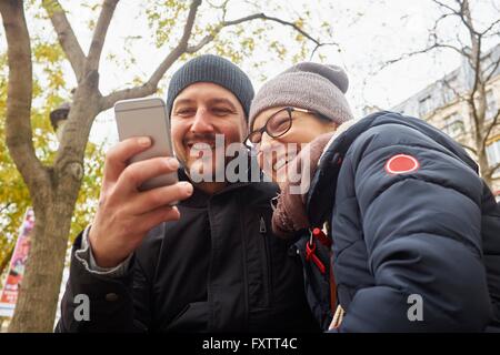Couple wearing knit hats in park reading smartphone texts Stock Photo