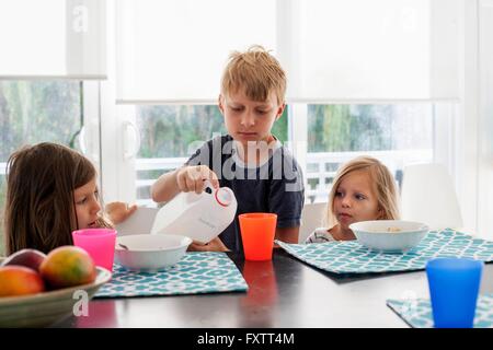 Big brother pouring milk into sisters plastic cup Stock Photo