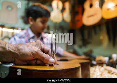 Small family business and traditions: old grandpa with grandson in lute maker shop. The senior artisan teaches how to tune a cla Stock Photo