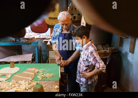 Small family business and traditions: old grandpa with grandson in lute maker shop. The senior artisan teaches to the boy how to Stock Photo