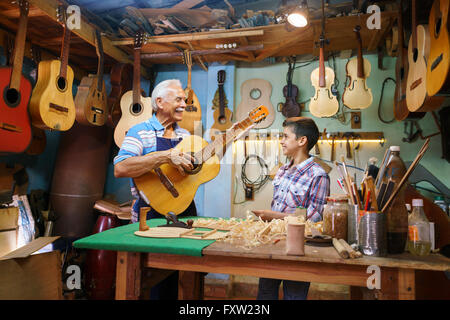 Small family business and traditions: old grandpa with grandson in lute maker shop. The senior artisan gives teaches how to play Stock Photo