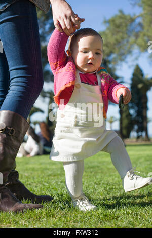 Cute baby girl learning to walk over the grass park on springtime Stock Photo