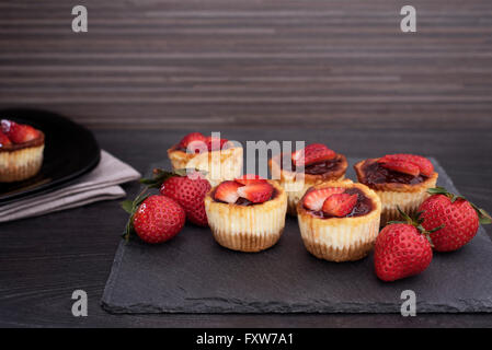 Mini strawberry cheesecake in muffin forms. Served in black stone plateau with fresh strawberries. Black wood background. Stock Photo