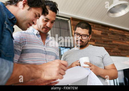Three coworkers having a discussion on business proposal in office. Focused creative young people going through documents togeth Stock Photo