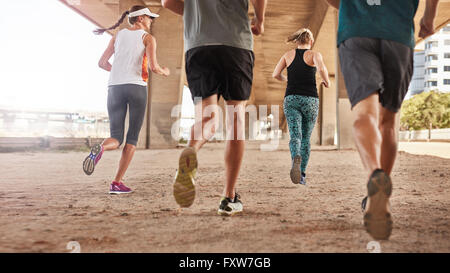 Rear view of young people running under the bridge in the city. Low angle shot of group of young men and women jogging together.