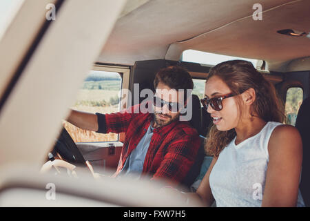 Young couple sitting inside their car and looking at something interesting. Young man and woman sitting together and looking at Stock Photo