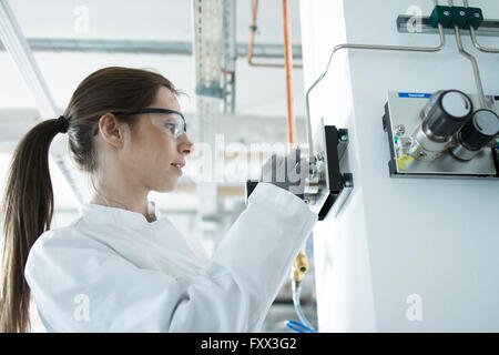 Side view of woman in workshop wearing safety goggles and coat adjusting control panel Stock Photo