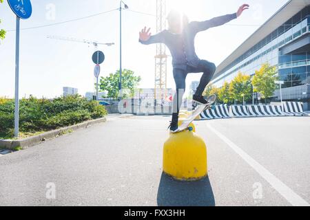 Young male urban skateboarder balancing on top of yellow bollard Stock Photo