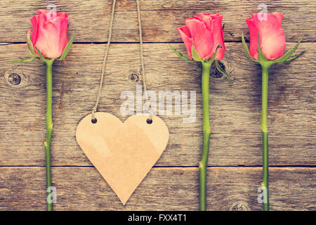 Blank heart shaped tag and roses on wooden background. Stock Photo
