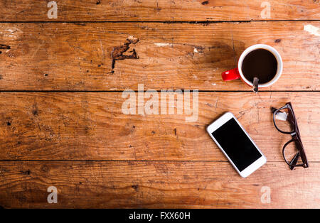 Smartphone, cup of coffee and eyeglasses on office desk Stock Photo