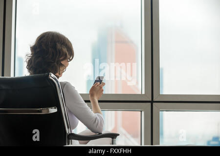 Back view of young successful business lady making call using smart phone. Model sitting in office comfortable armchair Stock Photo