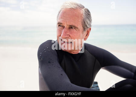 Happy senior man in wetsuit sitting on beach Stock Photo