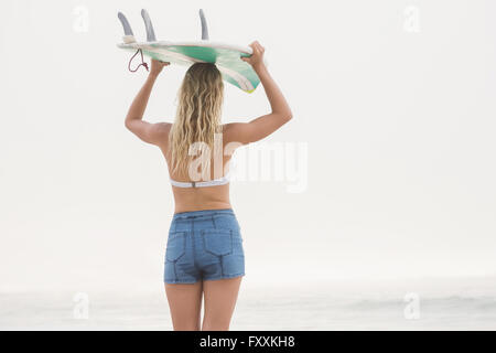 Pretty blonde woman holding a surfboard over her head Stock Photo