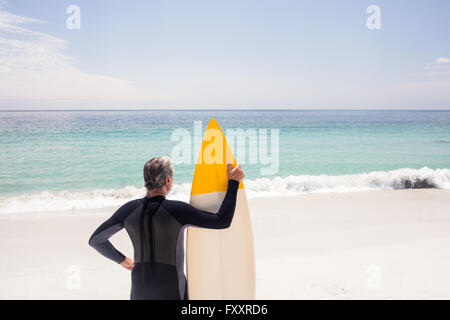 Rear view of senior man in wetsuit holding a surfboard Stock Photo