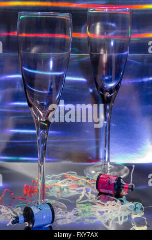 A Studio Photograph of Two Champagne Flutes and Party Poppers Set Against a Silver Holographic Backdrop Stock Photo