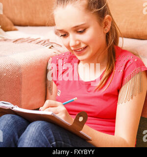 Young happy smiling teenager girl writing in diary notebook sitting on floor Stock Photo