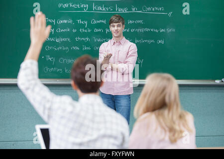 Foreign teacher and students listening to his lecture and one of them raising his hand up in class in college Stock Photo
