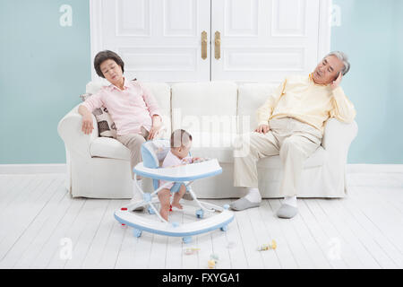 Grandparents seated on a couch feeling tired of taking care of a baby Stock Photo