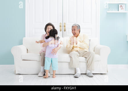 Senior couple seated on a couch and hugging their granddaughter with a smile Stock Photo