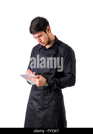 Young chef or waiter posing, wearing black apron and shirt, writing order on notepad, isolated on white background Stock Photo