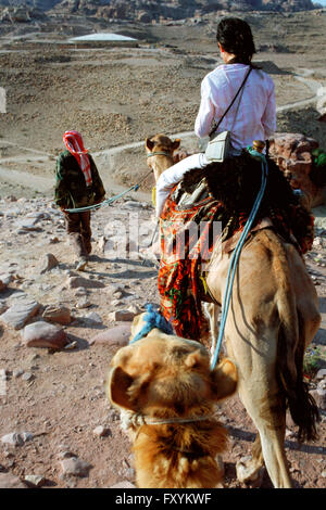 Bedouin guide with tourist girl in a camel ride, Petra, Jordan. Stock Photo