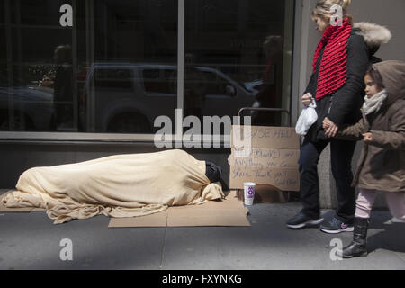 Homeless person sleeps on the sidewalk in midtown Manhattan as people pass by. Stock Photo