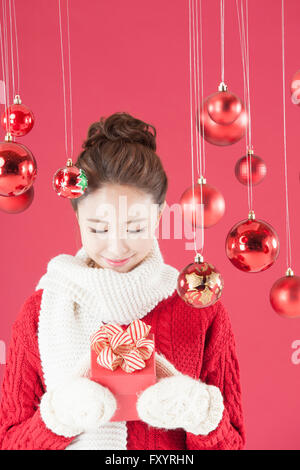 Portrait of young smiling woman wearing muffler and mittens looking down at present box inher hands with Christmas balls Stock Photo